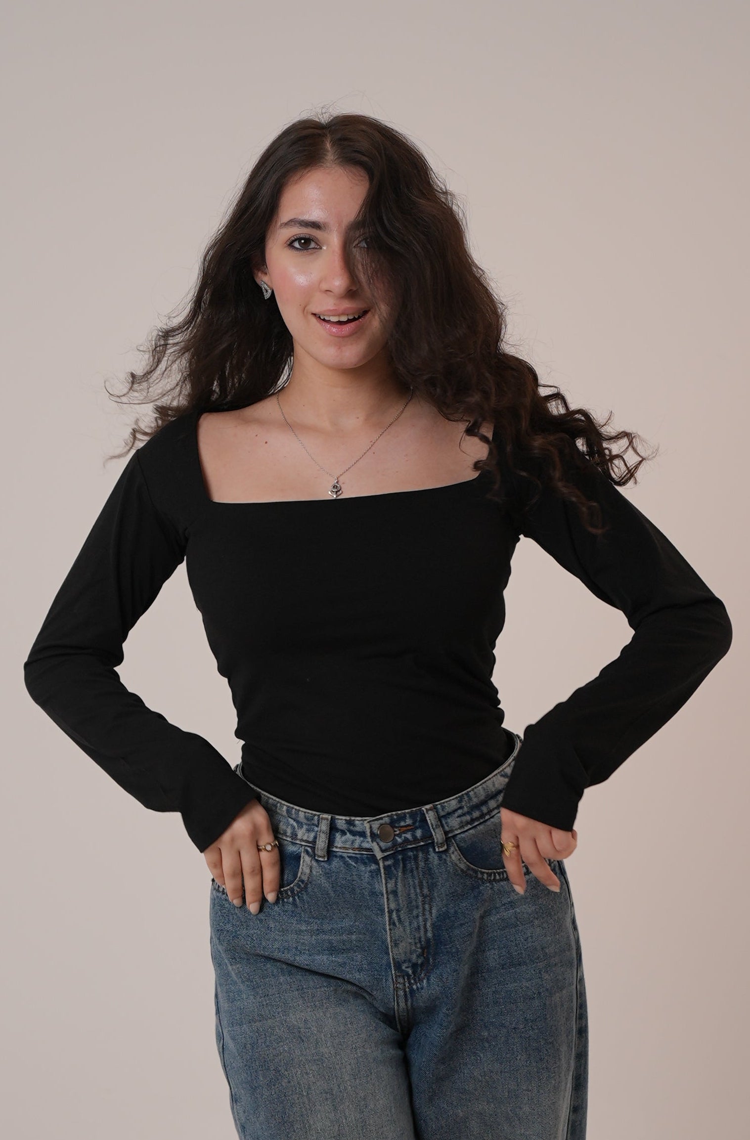 Person wearing a black long-sleeve top and blue jeans on a plain background